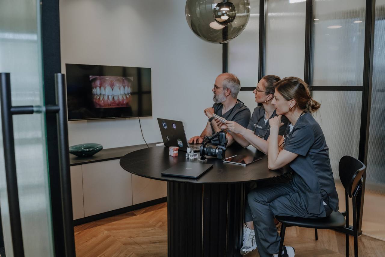 Drei Zahnärzte werten gemeinsam Befundbilder an einem Wandmonitor aus